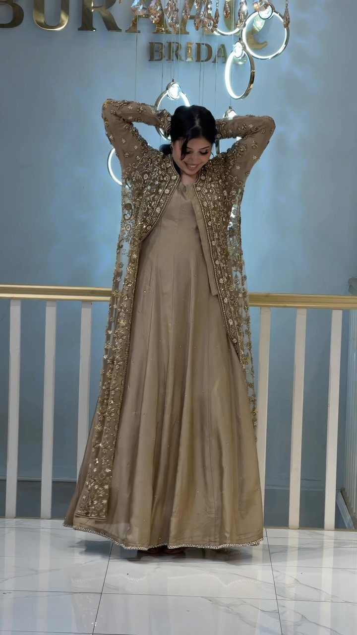 A woman posing in a gold embellished jacket over a long champagne-colored gown.