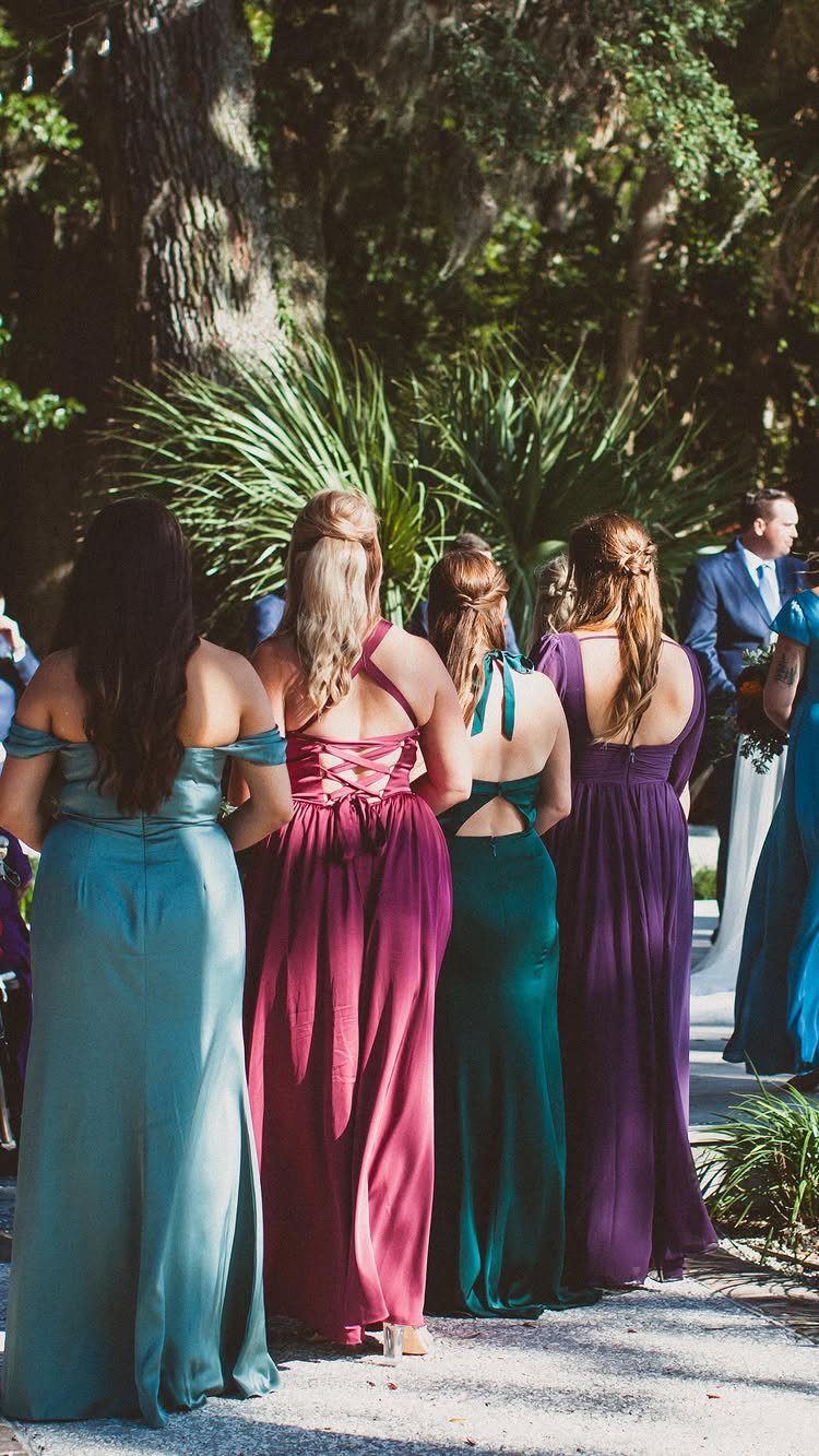 Four women in colorful formal gowns standing outdoors with their backs to the camera.