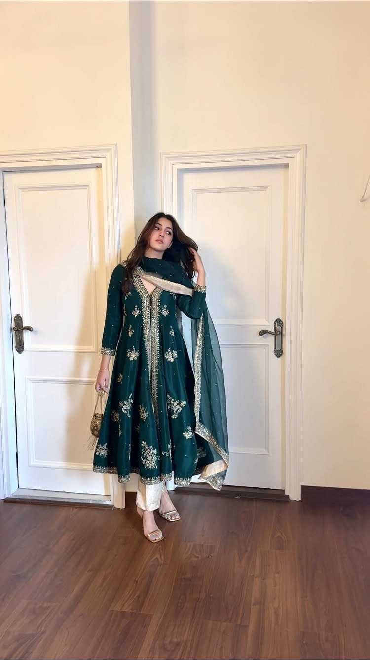 Woman posing in a dark green velvet embroidered anarkali suit with a matching dupatta.
