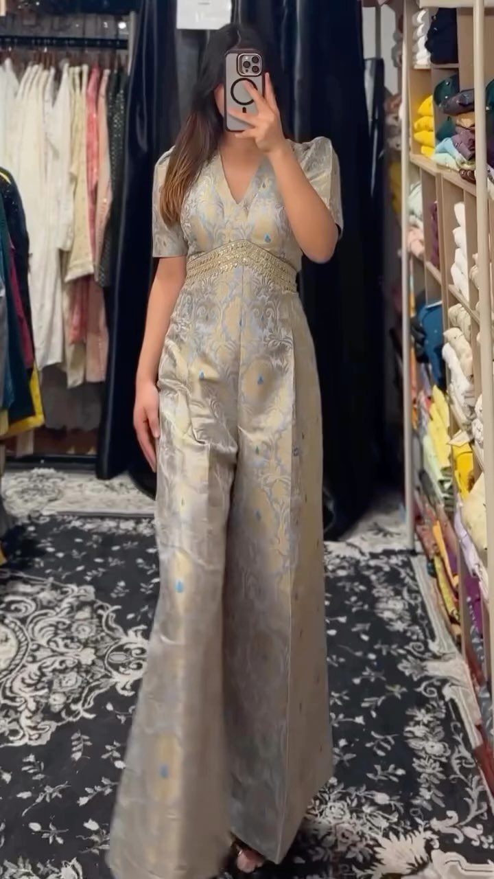 A woman posing in a gold patterned jumpsuit while taking a mirror selfie.