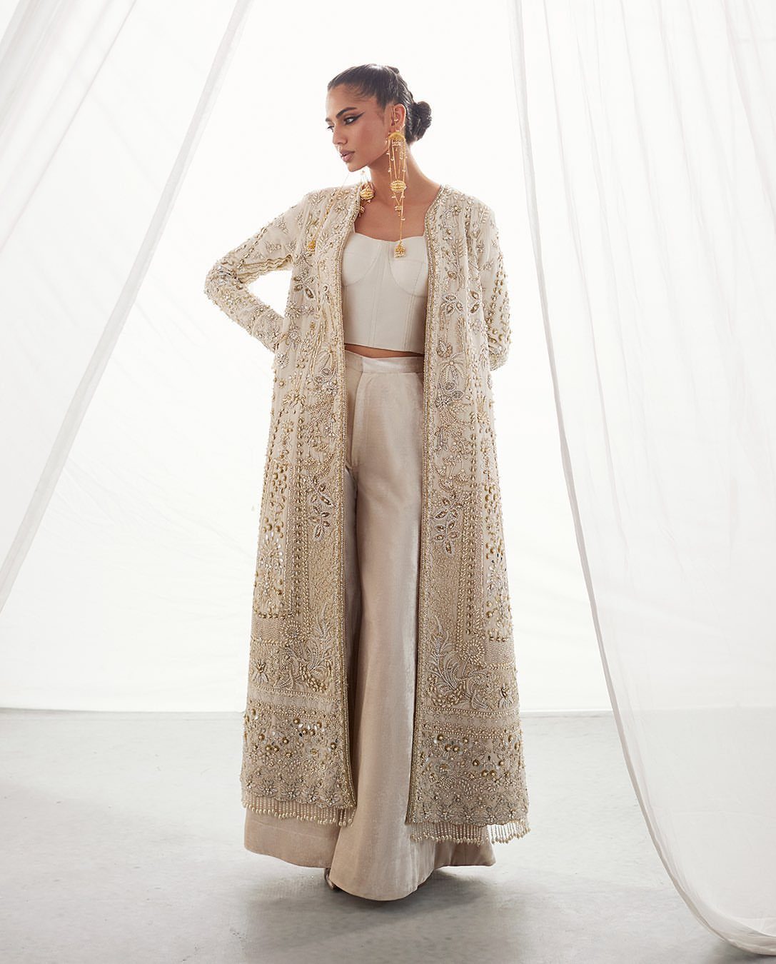 Woman wearing an embellished cream lace coat with matching crop top and wide-leg trousers.