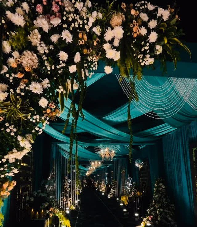 25 Wedding Stuff Ideas for Your 2026 Ceremony and Party 16 Floral installations and teal fabric draping create a grand entrance walkway with hanging crystals.