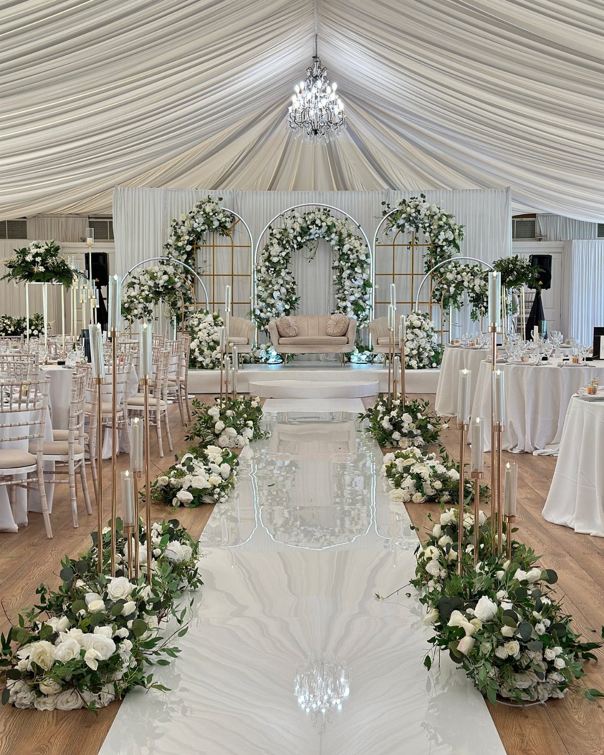 25 Wedding Stuff Ideas for Your 2026 Ceremony and Party 2 White wedding aisle lined with lush greenery and white floral arrangements under a draped tent.