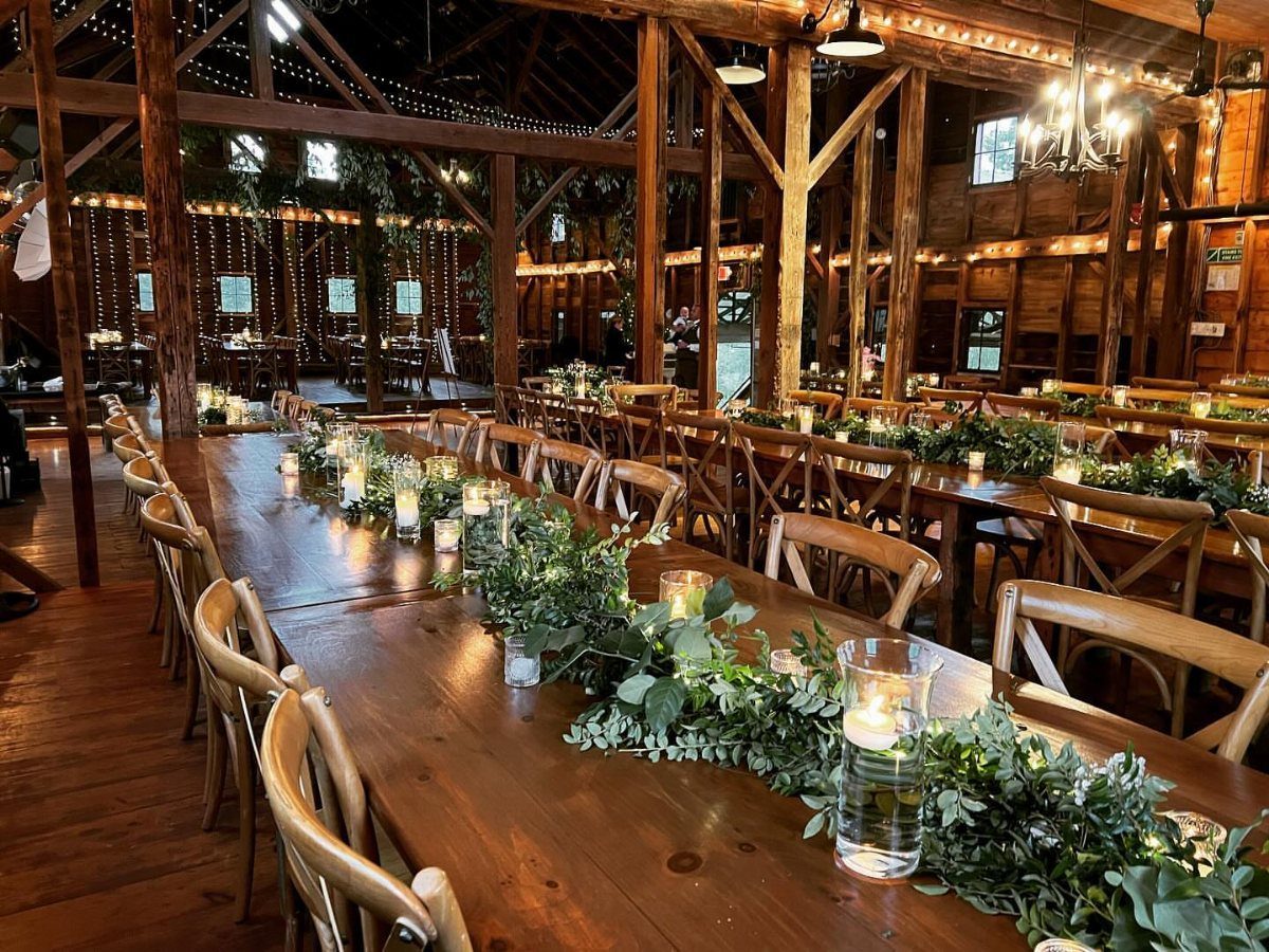 25 Wedding Stuff Ideas for Your 2026 Ceremony and Party 21 Long wooden tables decorated with green foliage runners and white candles in a rustic barn.
