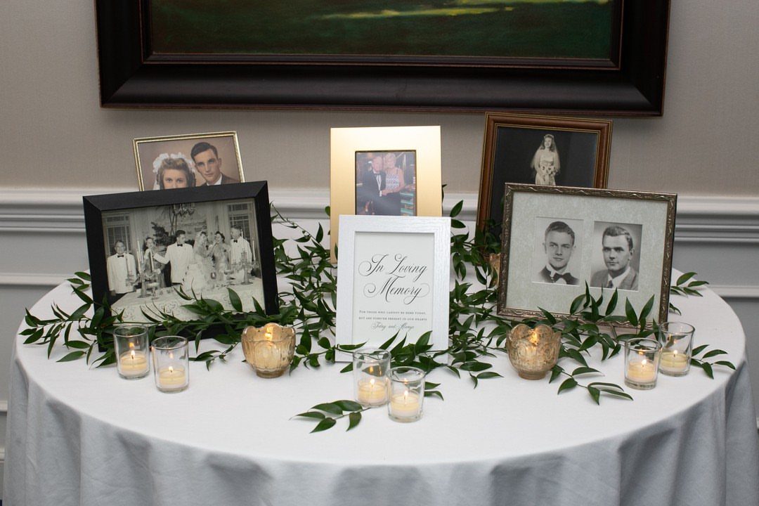 25 Wedding Stuff Ideas for Your 2026 Ceremony and Party 15 Framed black and white photographs and greenery arranged on a white tablecloth with memorial signage.