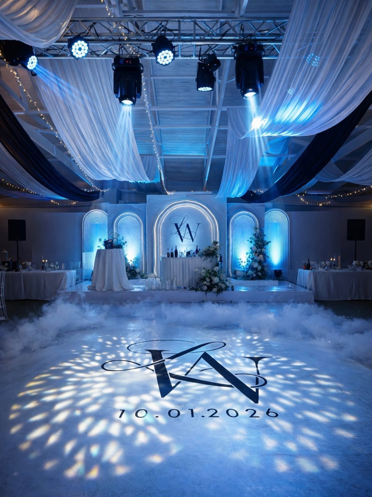 25 Wedding Stuff Ideas for Your 2026 Ceremony and Party 20 A wedding reception hall with blue lighting, white fabric draping, and a monogram projected on the dance floor.