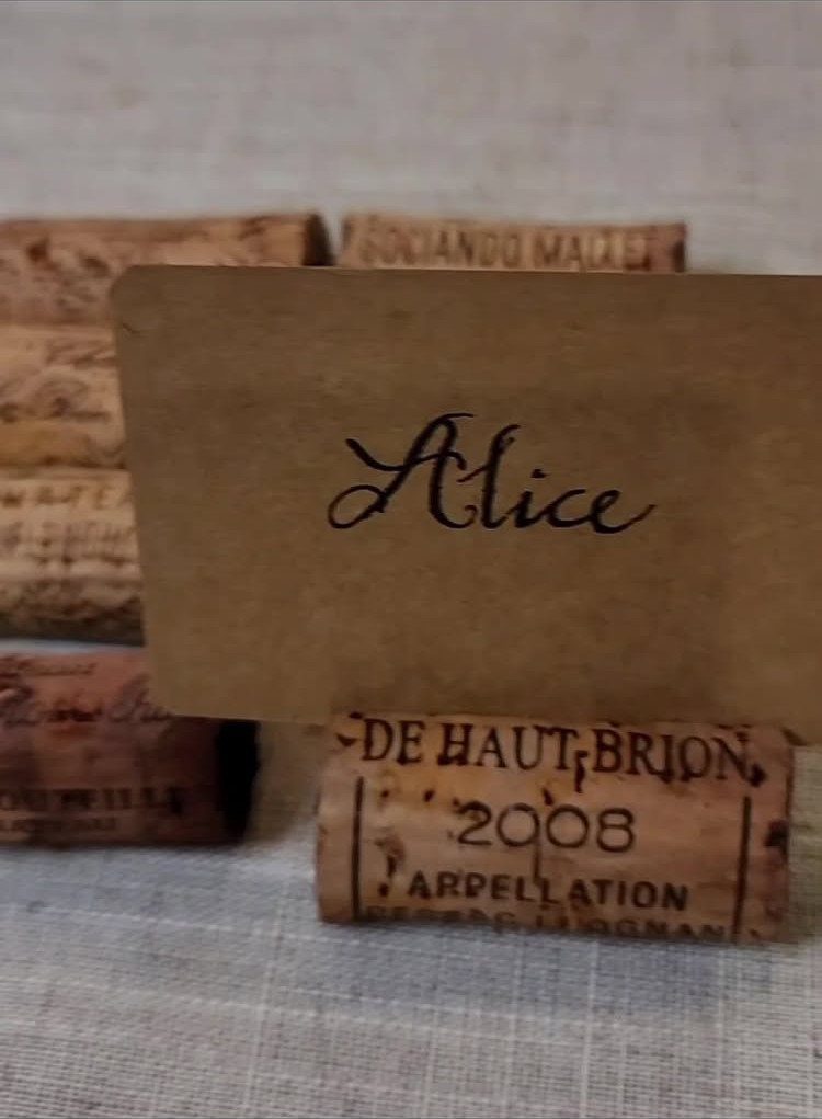 25 Wedding Stuff Ideas for Your 2026 Ceremony and Party 11 Wine corks and a small place card with the name Alice on a linen surface.