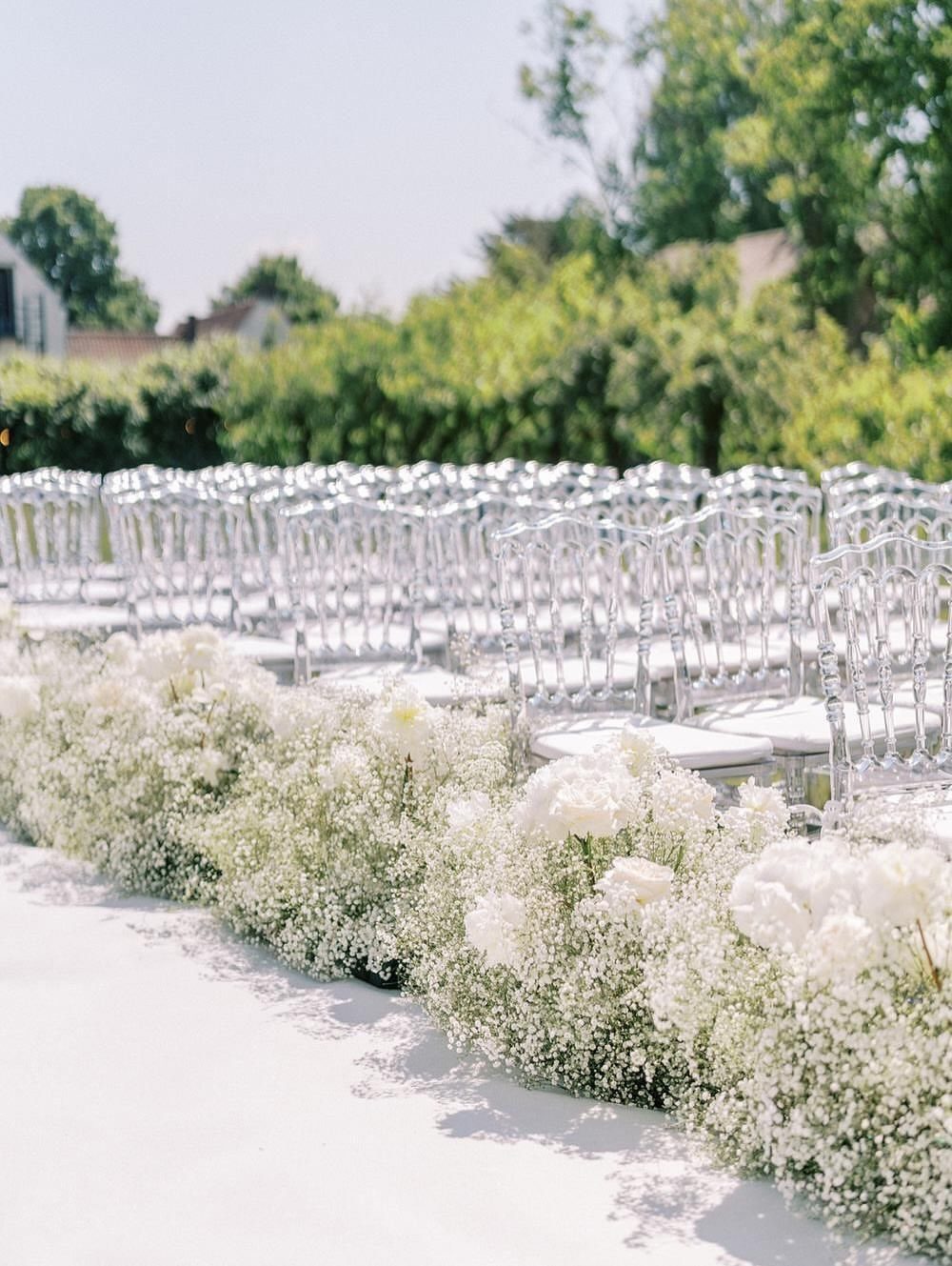 Wedding Theme Flowers: 21 Ideas for Ceremony to Cake 16 White baby's breath flowers lining a white aisle runner at an outdoor wedding ceremony.