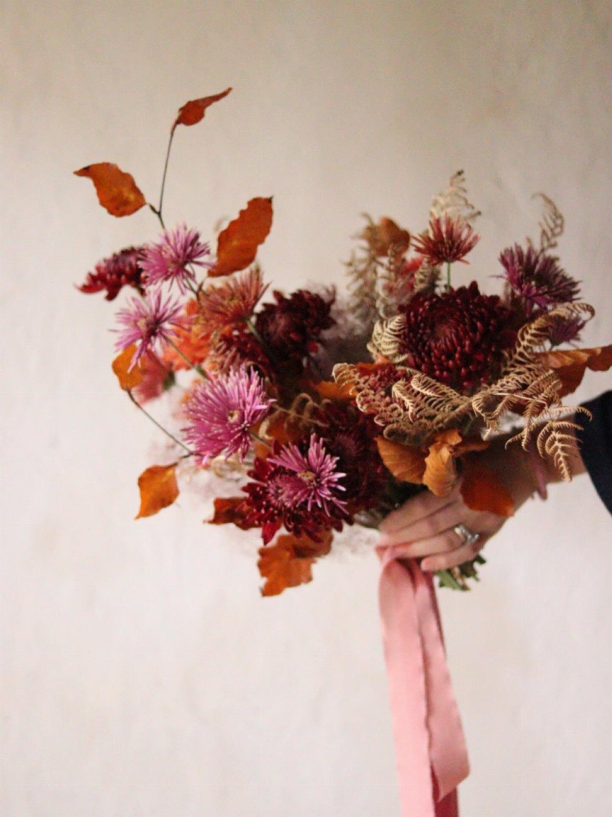 Wedding Theme Flowers: 21 Ideas for Ceremony to Cake 15 A hand holding a bouquet of colorful chrysanthemums and autumn leaves with a pink ribbon.