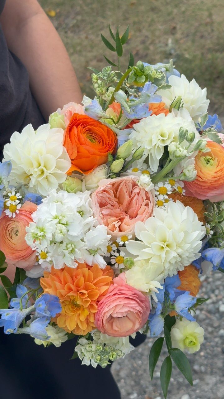 Wedding Theme Flowers: 21 Ideas for Ceremony to Cake 12 A colorful wedding bouquet with orange dahlias, peach ranunculus, and blue sweet peas.