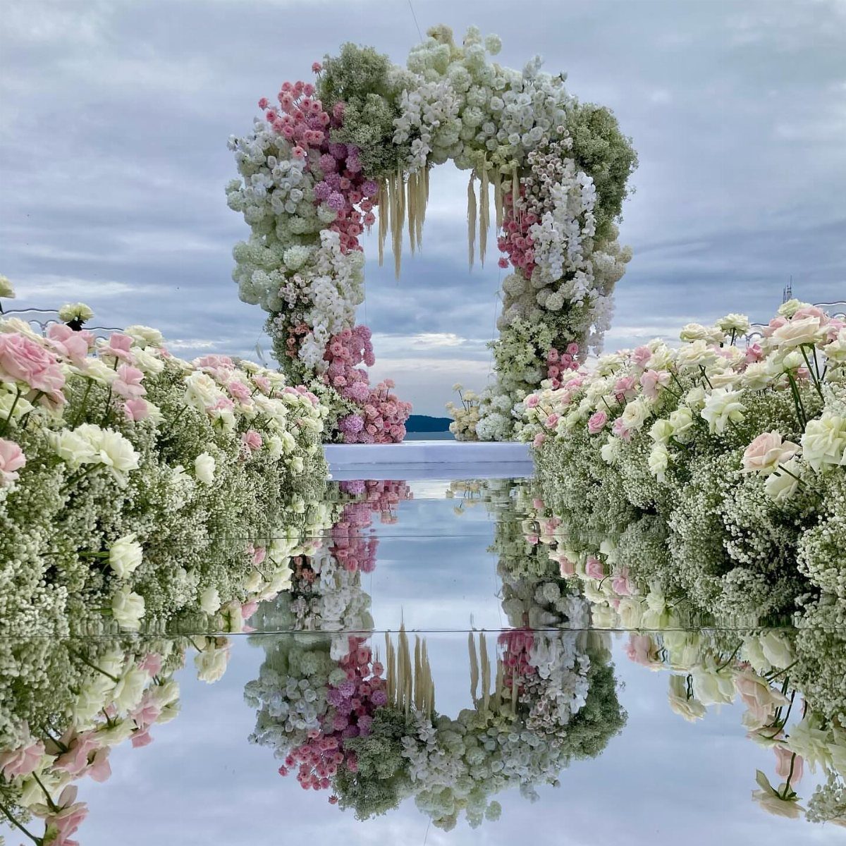 Wedding Theme Flowers: 21 Ideas for Ceremony to Cake 21 A large floral arch with pink and white flowers reflected on a glossy surface.