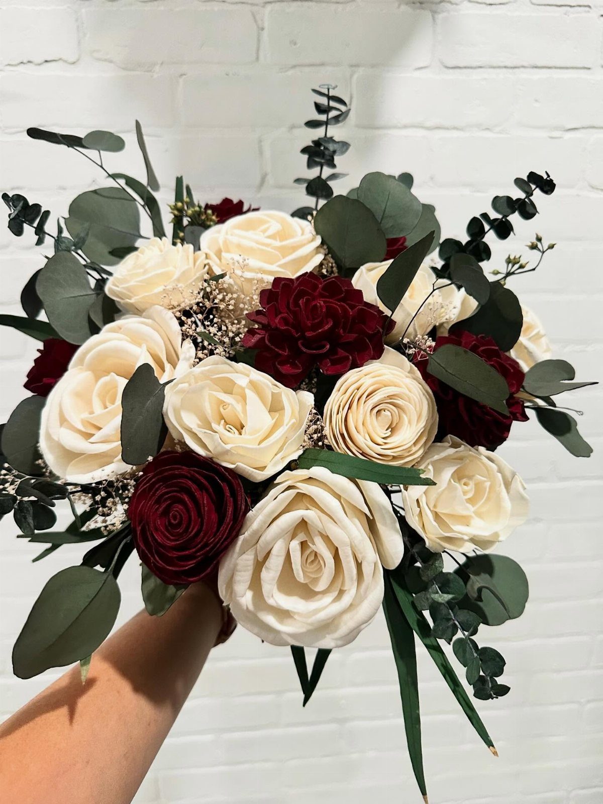 Wedding Theme Flowers: 21 Ideas for Ceremony to Cake 17 A hand holding a bouquet of cream and burgundy sola wood flowers with eucalyptus leaves.