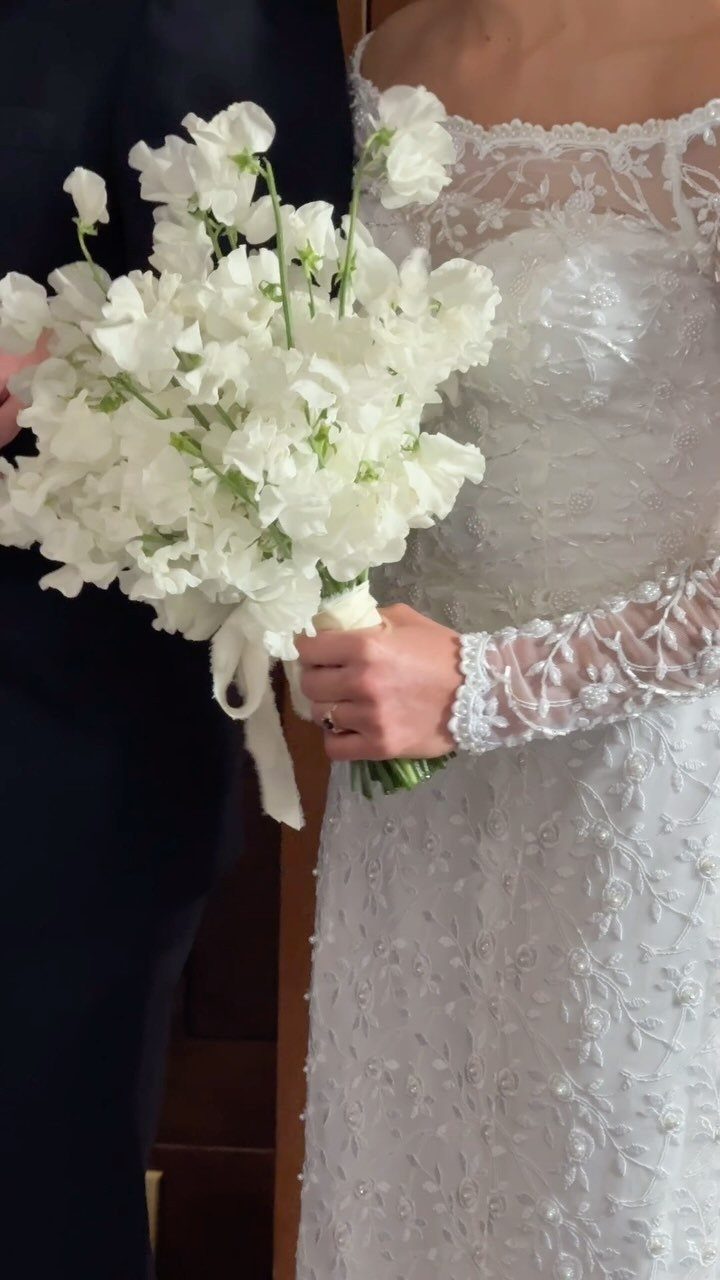 Wedding Theme Flowers: 21 Ideas for Ceremony to Cake 5 A bride holding a large bouquet of white sweet pea flowers against her lace dress.