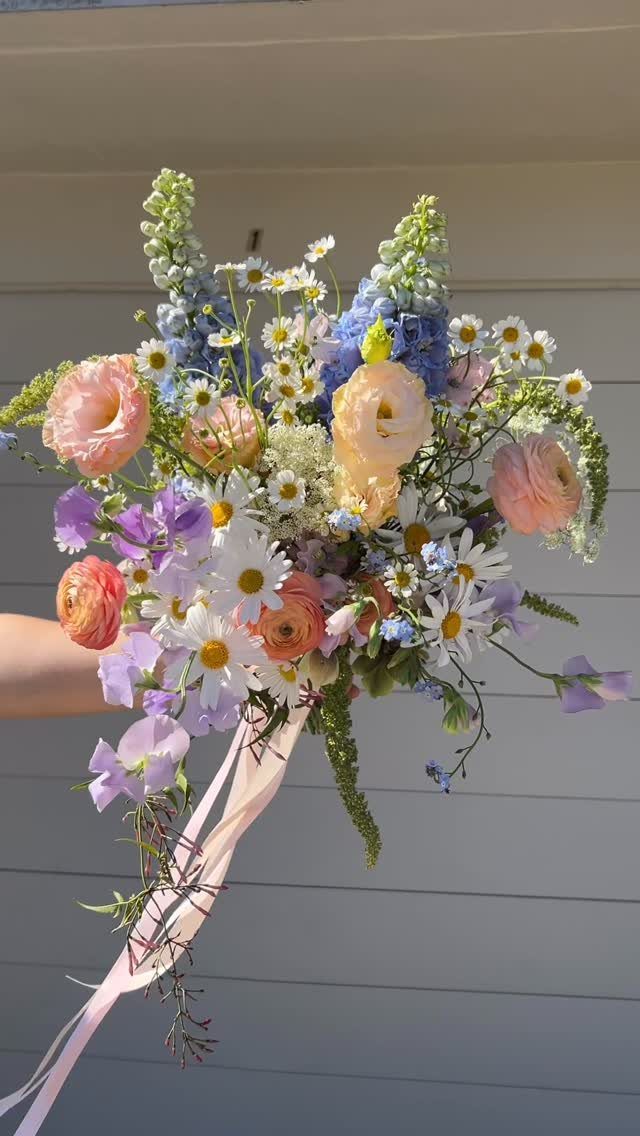 Wedding Theme Flowers: 21 Ideas for Ceremony to Cake 7 A colorful bridal bouquet with ranunculus, daisies, and blue wildflowers tied with pink ribbon.