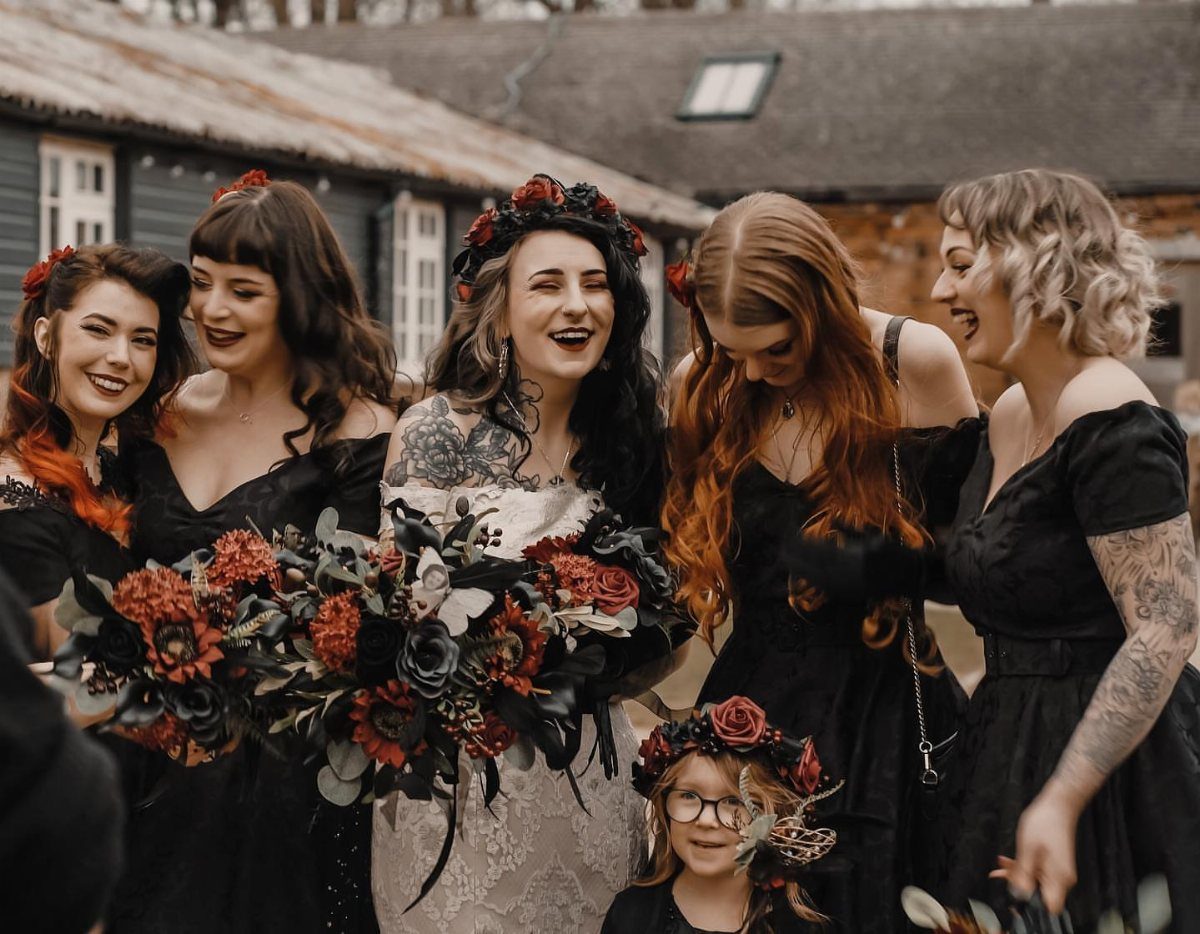 Wedding Theme and Motif: 16 Fresh Ideas for 2026 13 Bridesmaids and a bride in black dresses holding a dark floral bouquet outdoors.