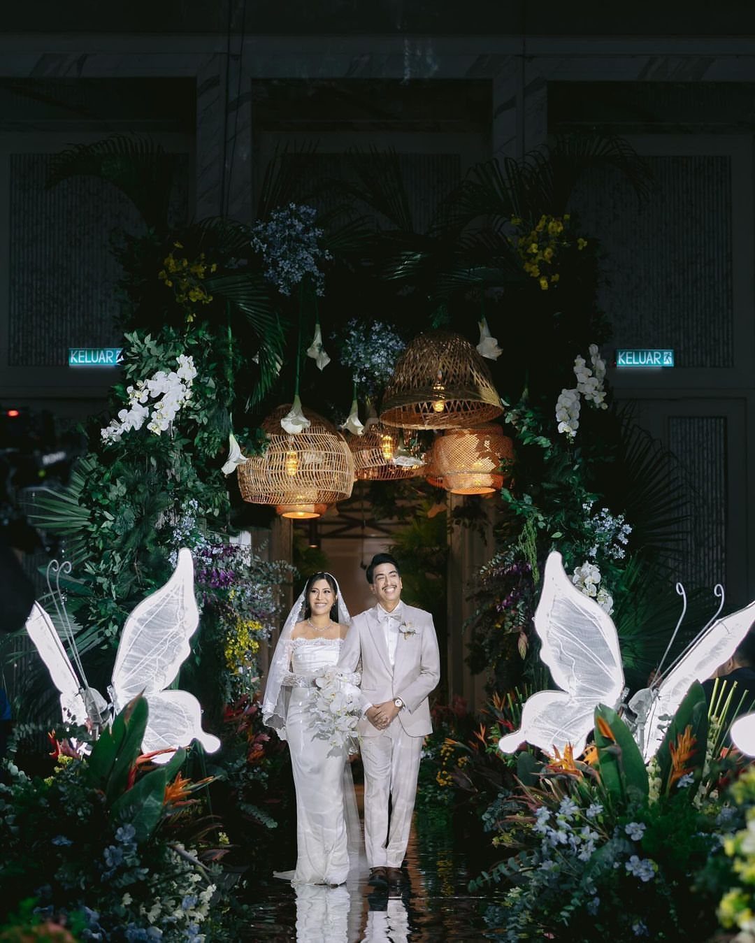 Wedding Theme and Motif: 16 Fresh Ideas for 2026 5 A bride and groom posing amidst lush tropical greenery and glowing butterfly decorations.