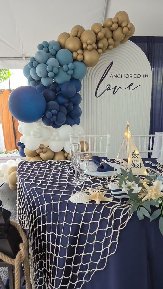 Wedding Theme and Motif: 16 Fresh Ideas for 2026 6 A wedding table decorated with a navy tablecloth, fishing net, starfish, and seashells under a balloon arch.