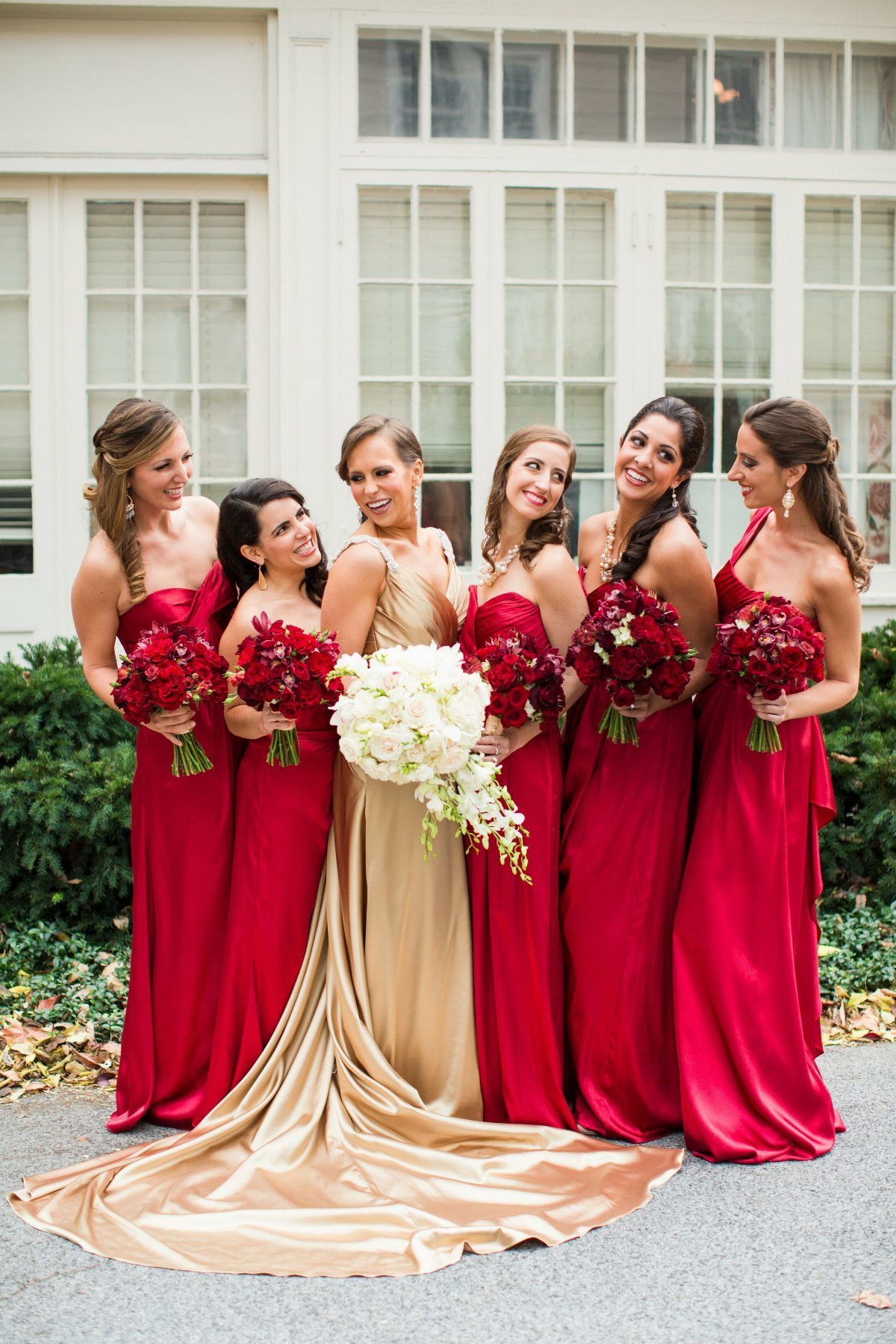 8 Wedding Theme Red and Gold Ideas for Every Part of Your Day 3 A bride in gold and bridesmaids in red dresses holding floral bouquets outdoors.