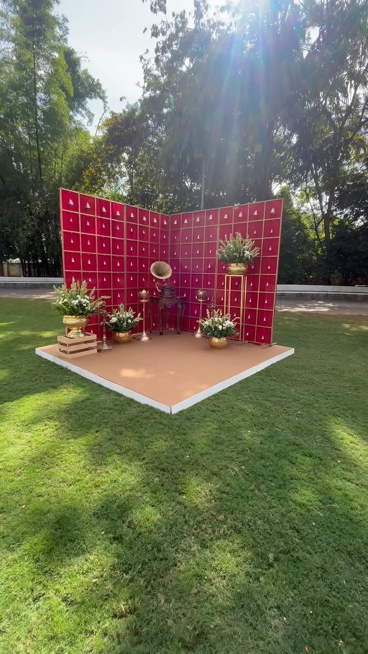 8 Wedding Theme Red and Gold Ideas for Every Part of Your Day 7 Red backdrop with gold grid pattern and floral arrangements on a platform outdoors.