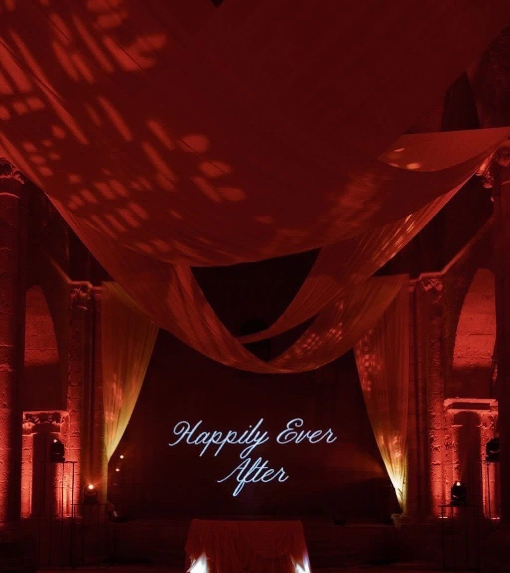 8 Wedding Theme Red and Gold Ideas for Every Part of Your Day 8 Red lit wedding reception hall with draped fabric and a neon sign reading Happily Ever After.