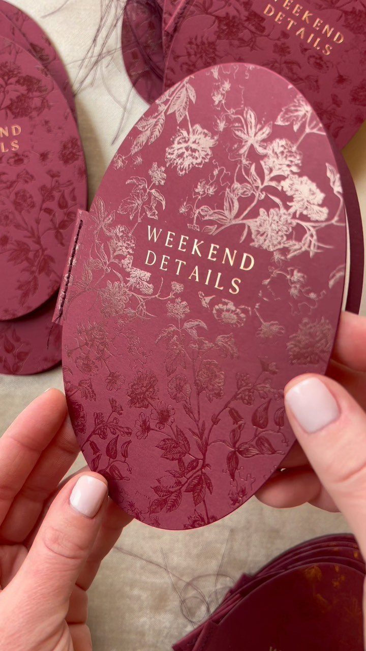 8 Wedding Theme Red and Gold Ideas for Every Part of Your Day 9 Hands holding an oval burgundy wedding card with gold floral patterns and text.