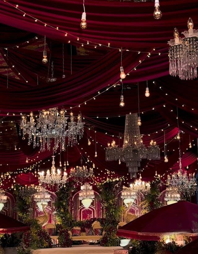 Wedding Themes 2026: 12 Ideas You Will Actually Want to Steal 11 Crystal chandeliers and warm lights hang from draped red fabric ceilings in a grand wedding venue.