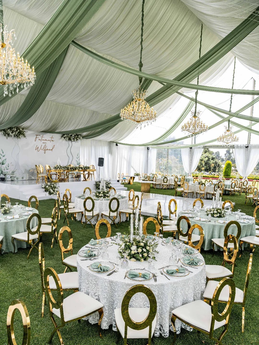 Wedding Themes 2026: 12 Ideas You Will Actually Want to Steal 2 Wedding reception tables with white lace cloths and floral centerpieces set on grass under a draped tent.