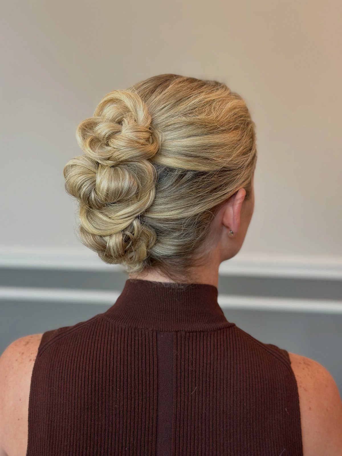27 Bridesmaid Wedding Updo Hairstyles from Buns to Braids 25 Blonde woman with an intricate textured updo bun wearing a brown top.