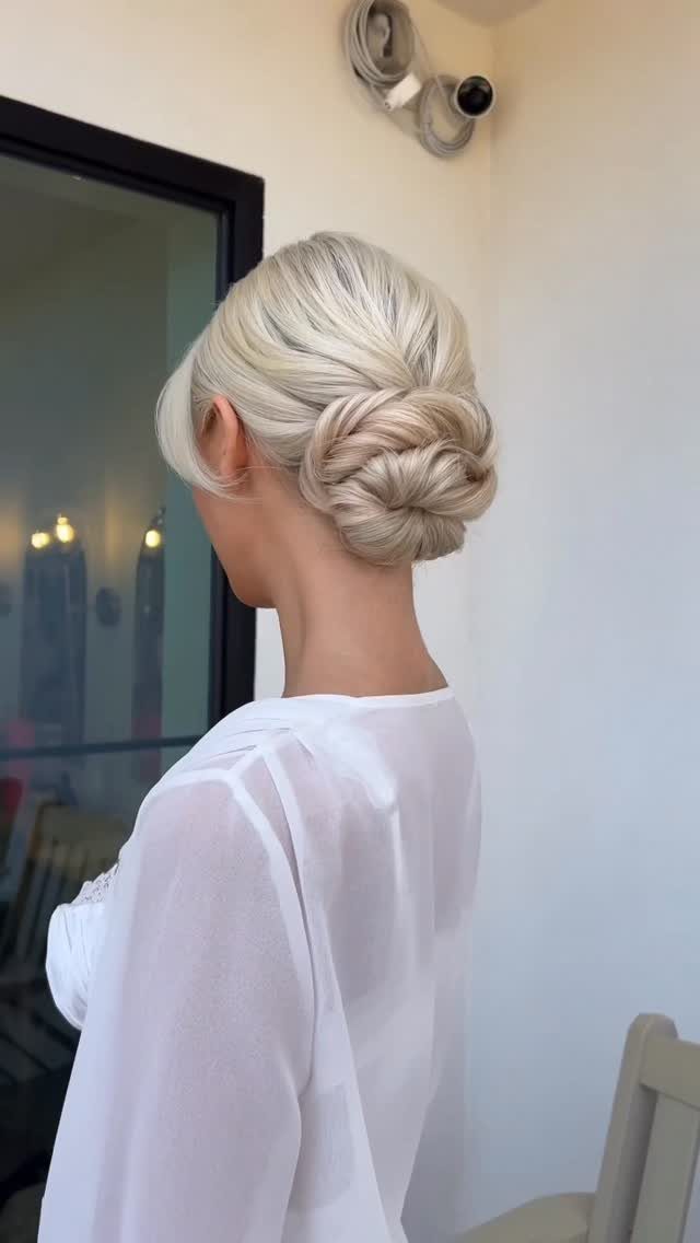 27 Bridesmaid Wedding Updo Hairstyles from Buns to Braids 18 Blonde woman with a polished low knot updo wearing a white sheer top.