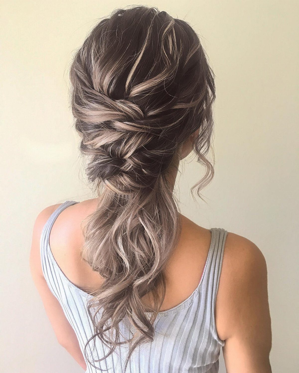 27 Bridesmaid Wedding Updo Hairstyles from Buns to Braids 8 Voluminous low ponytail with curls and twisted braids on brown highlighted hair.
