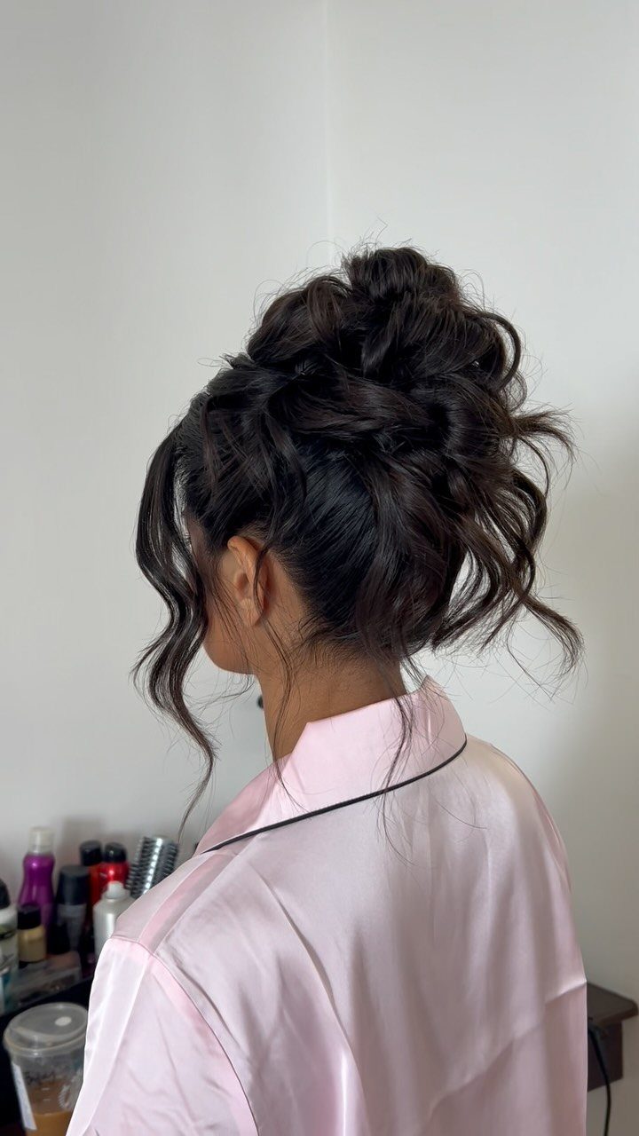 27 Bridesmaid Wedding Updo Hairstyles from Buns to Braids 5 Woman with a voluminous messy updo and loose curls wearing a pink robe.
