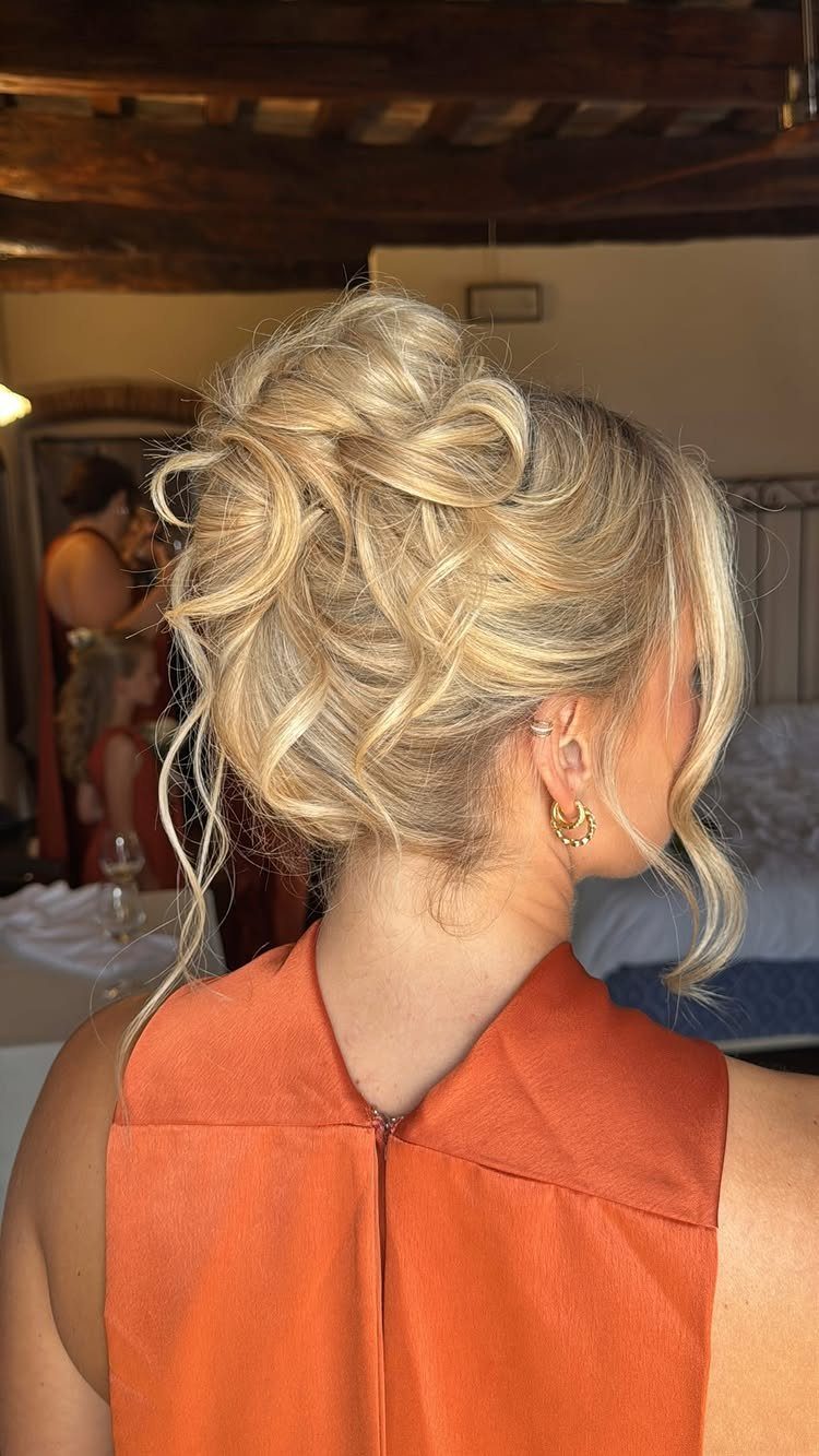 27 Bridesmaid Wedding Updo Hairstyles from Buns to Braids 9 Blonde woman with a voluminous curly updo and loose strands wearing orange dress.
