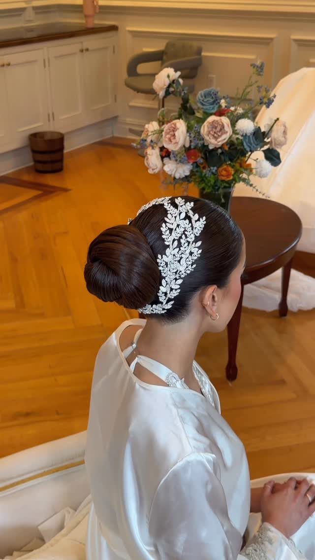 Wedding Updo Low Bun: How to Style 17 Beautiful Ideas 17 Woman with a polished low bun hairstyle and white floral hairpiece wearing a robe.