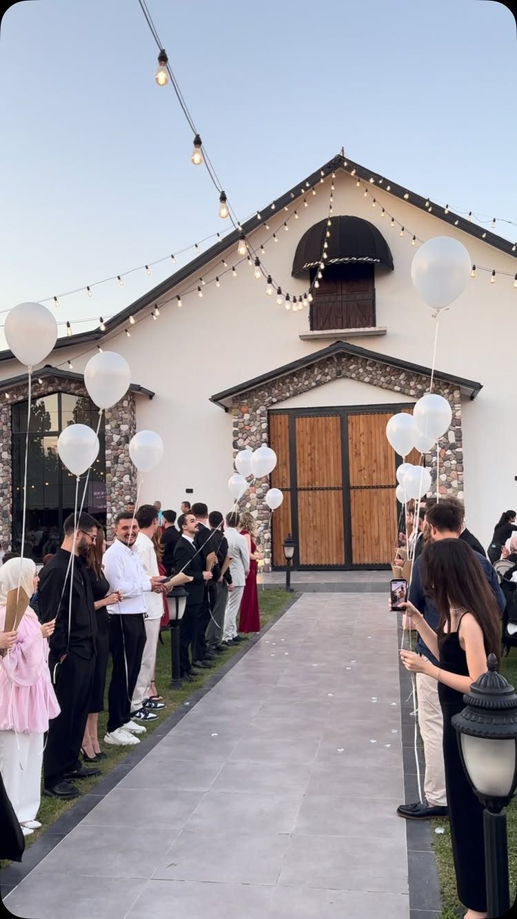 Guests with white balloons lining a stone path leading to wooden barn doors.
