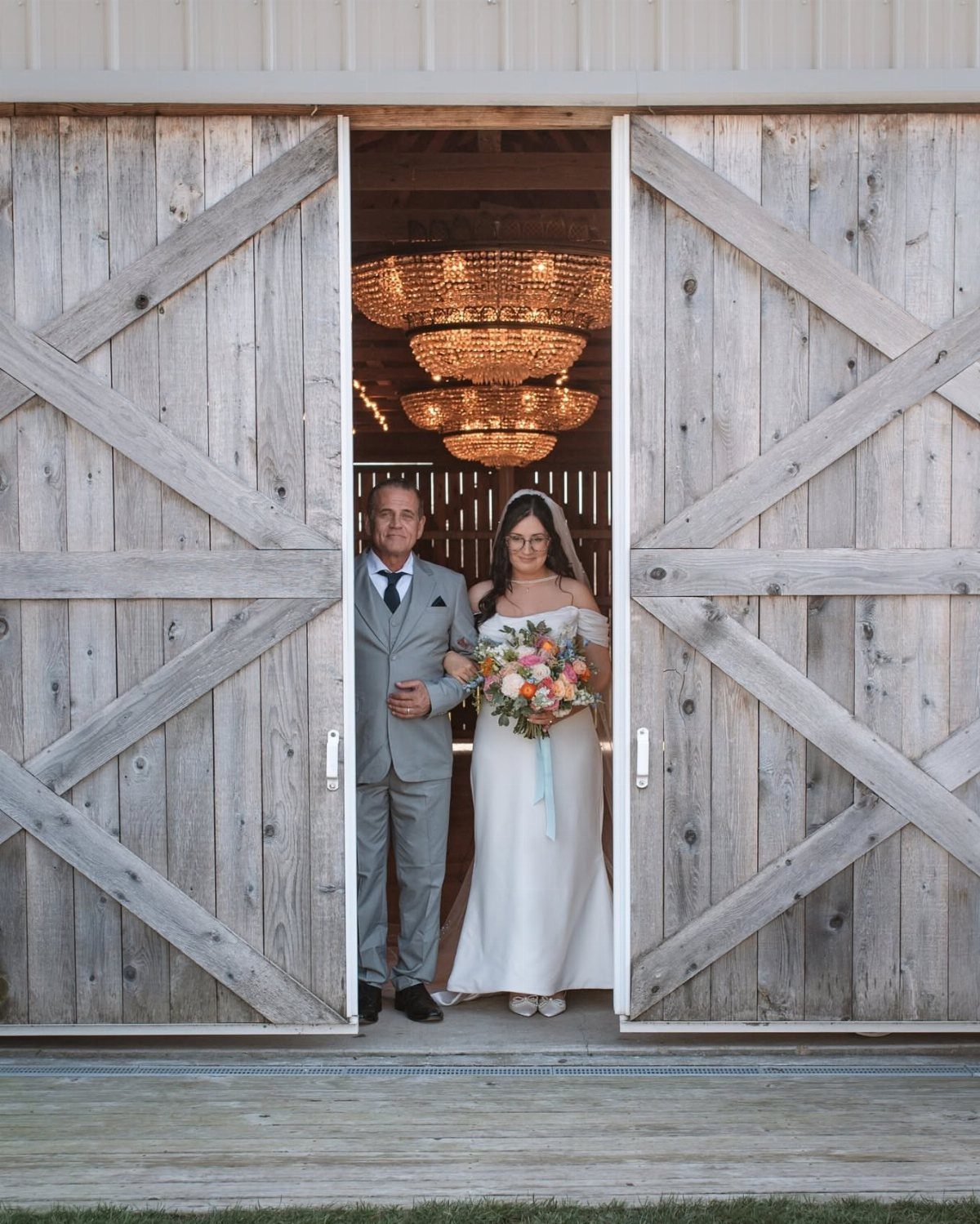 Bride and father standing in the open doorway of a rustic wooden barn
