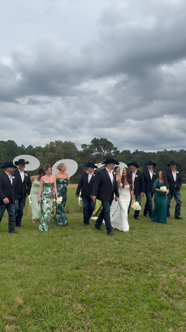 Wedding party in cowboy hats and gowns walking through a grassy field.