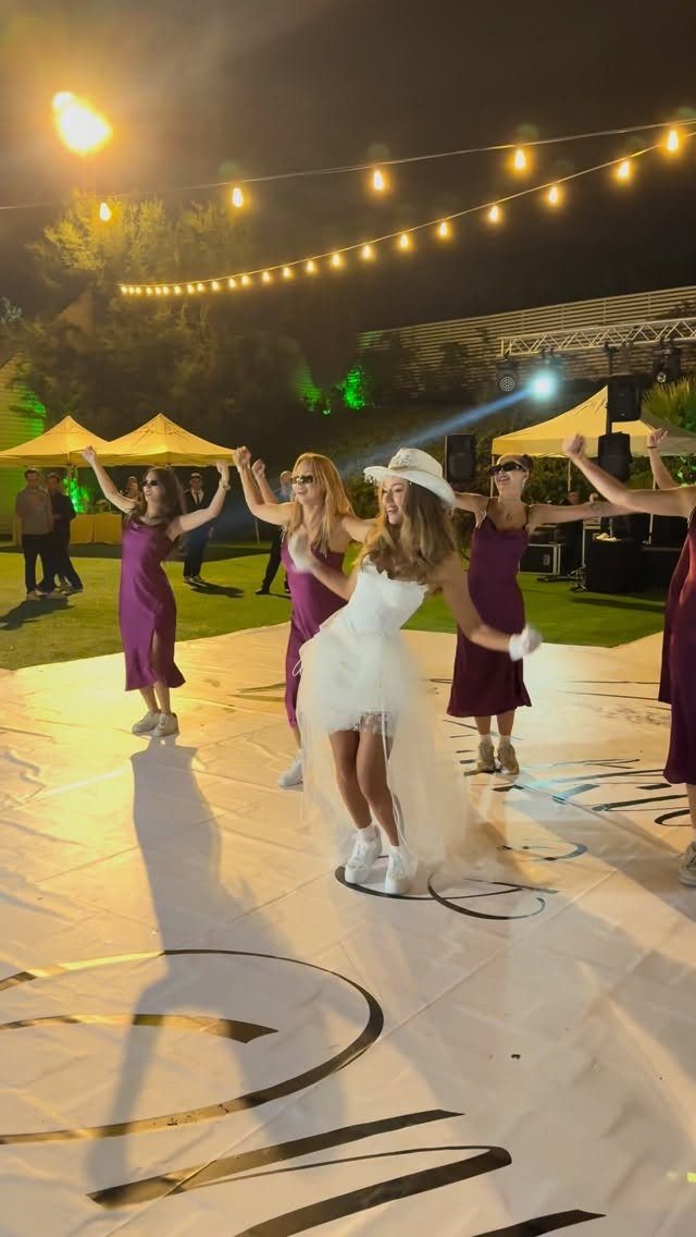 Bride and bridesmaids dancing on a white outdoor dance floor under string lights.