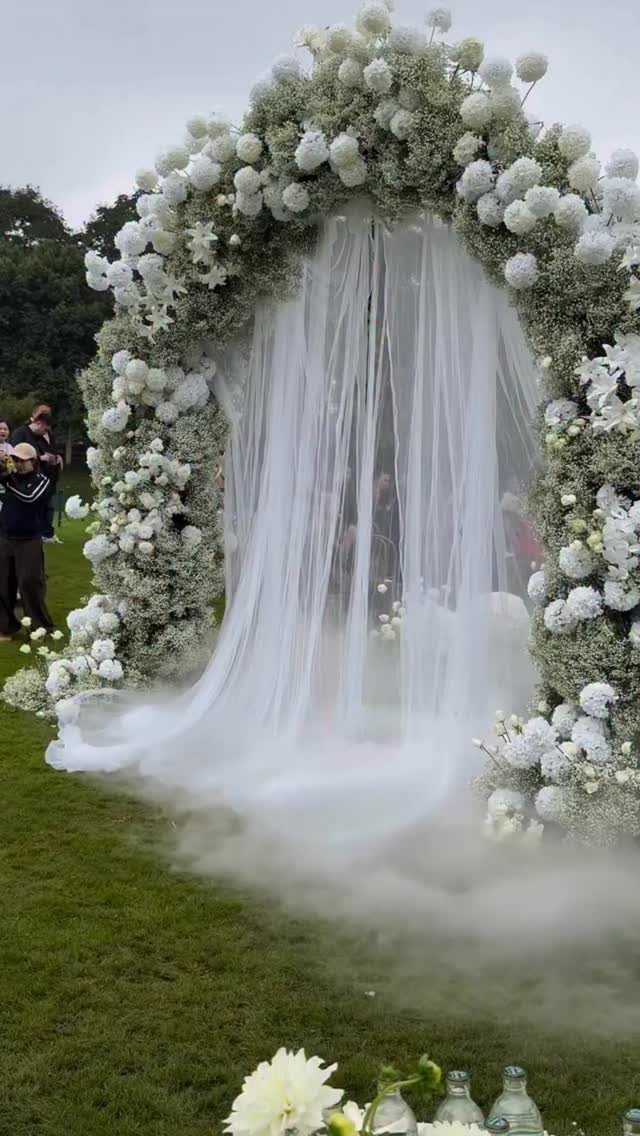 Floral arch with white curtains and low-lying fog on a green lawn