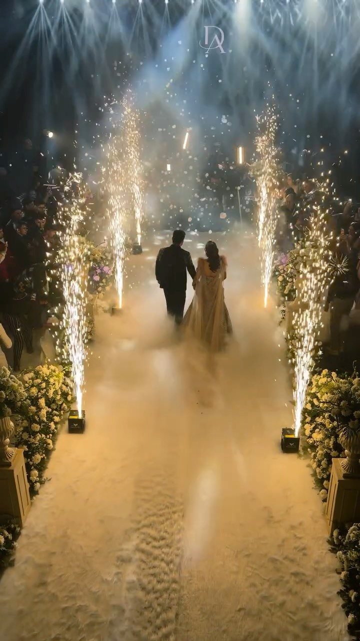 Bride and groom walking down a white aisle with indoor spark fountains.