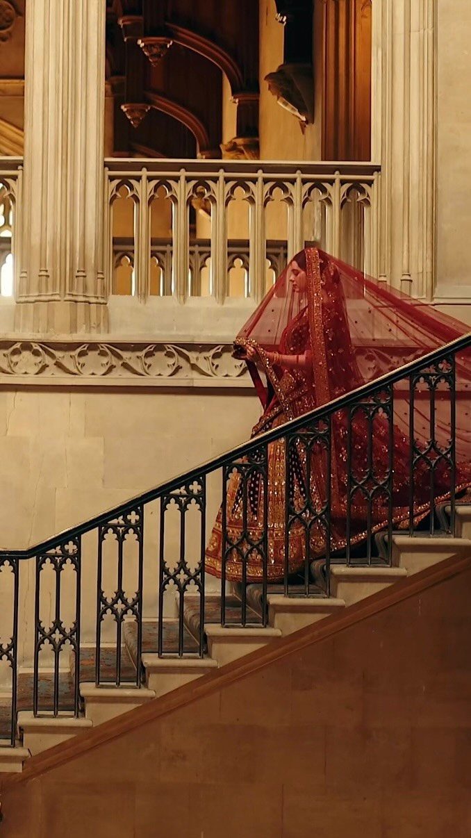 Bride in red traditional attire descending a grand stone staircase with ornate railings.