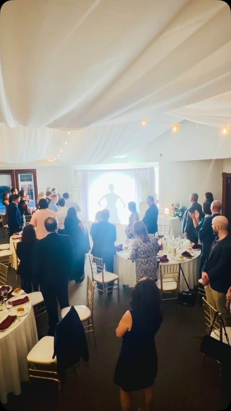 Bride's silhouette appearing in a bright doorway as guests watch at a wedding reception.