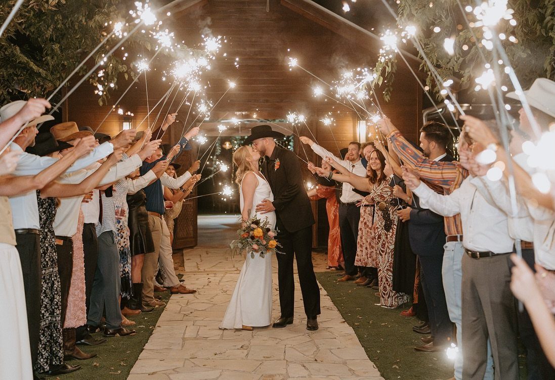 Bride and groom kissing while guests hold lit sparklers in a tunnel shape.
