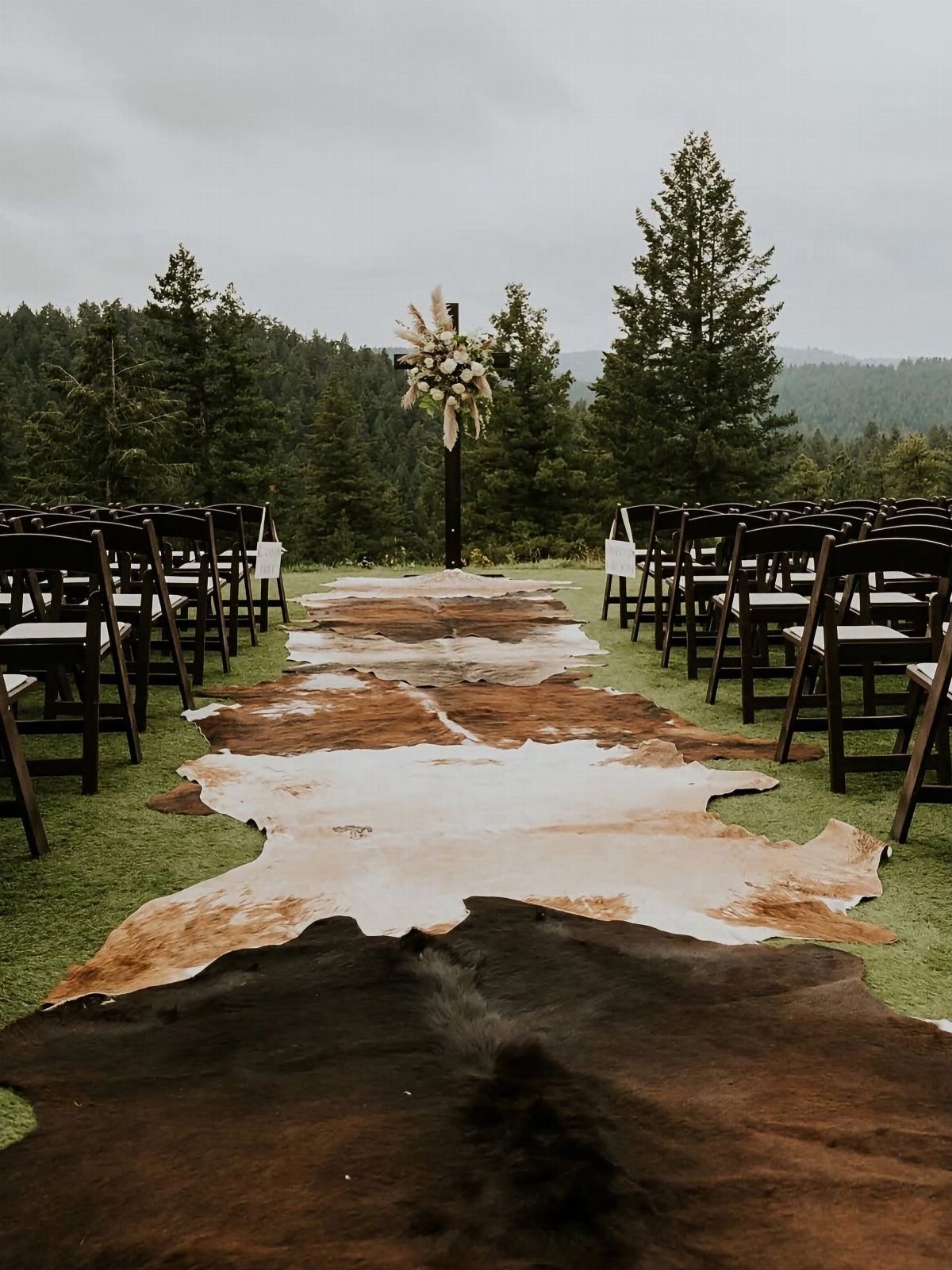 What Are the Best Western Themed Wedding Ideas? 37 Here 30 Cowhide rug aisle leading to a floral cross at an outdoor western wedding.