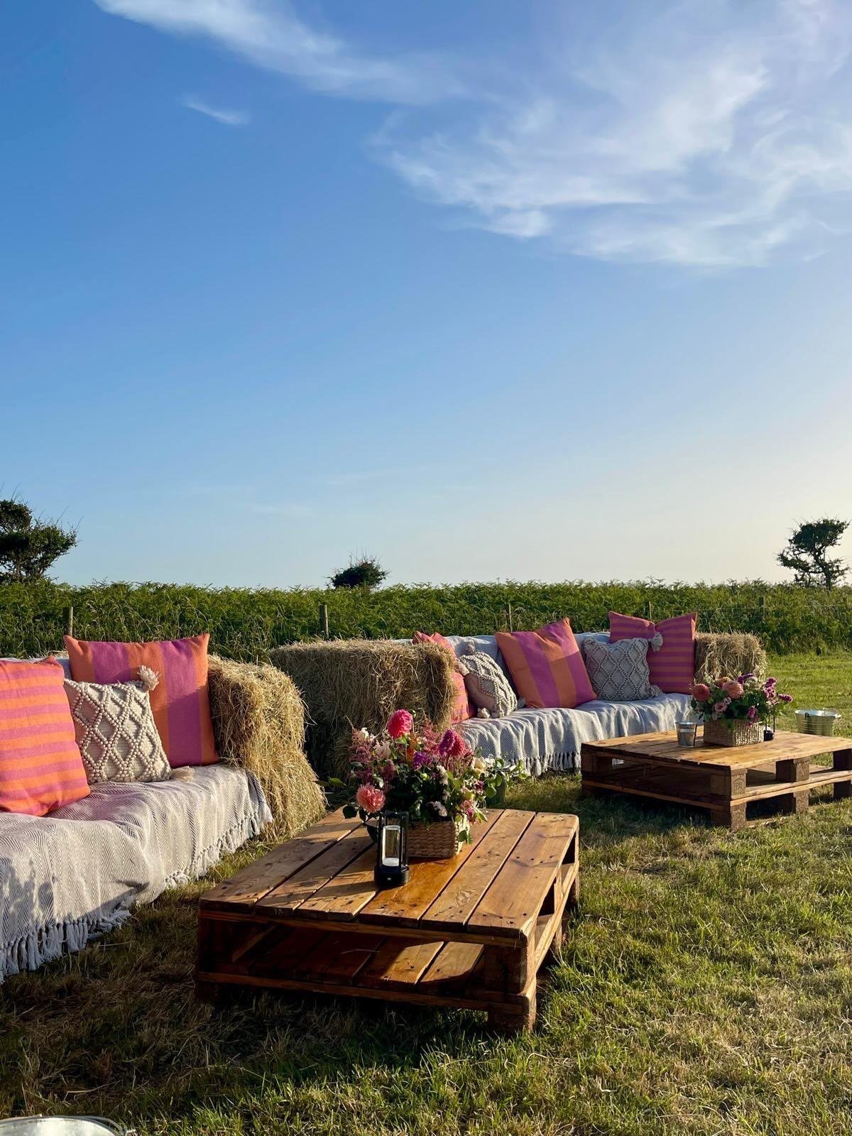What Are the Best Western Themed Wedding Ideas? 37 Here 13 Hay bale seating with pink pillows and wooden pallet tables in a field.