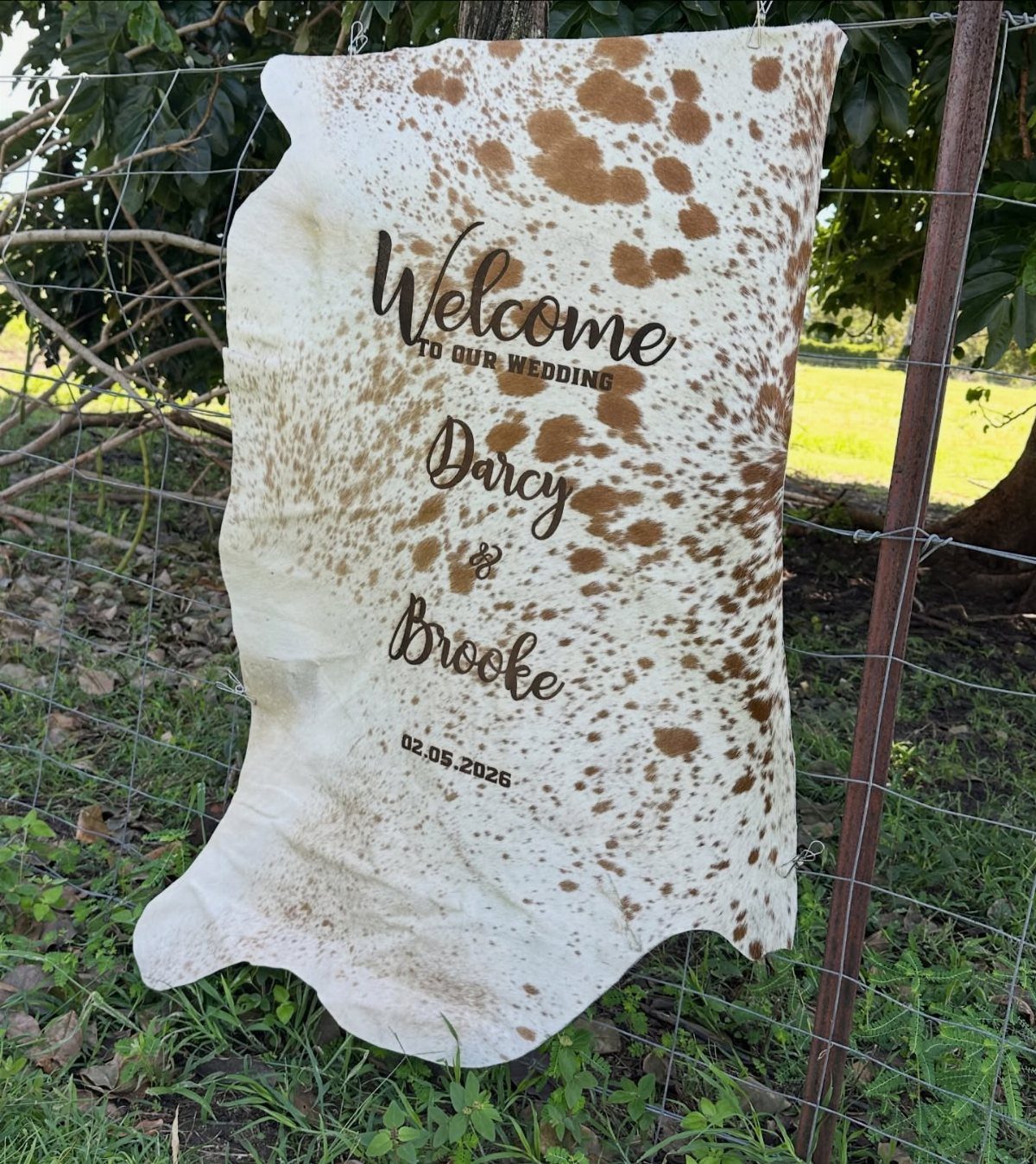 What Are the Best Western Themed Wedding Ideas? 37 Here 7 Cowhide wedding welcome sign with names and date hanging on a wire fence.