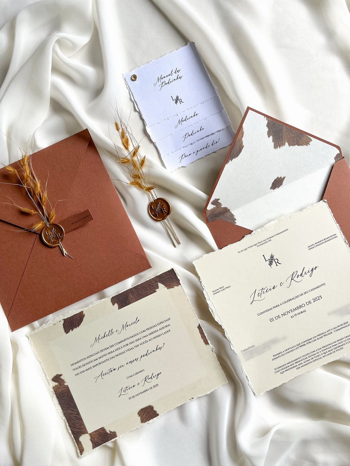 What Are the Best Western Themed Wedding Ideas? 37 Here 5 Wedding invitations with cowhide patterns and brown envelopes resting on white satin fabric.