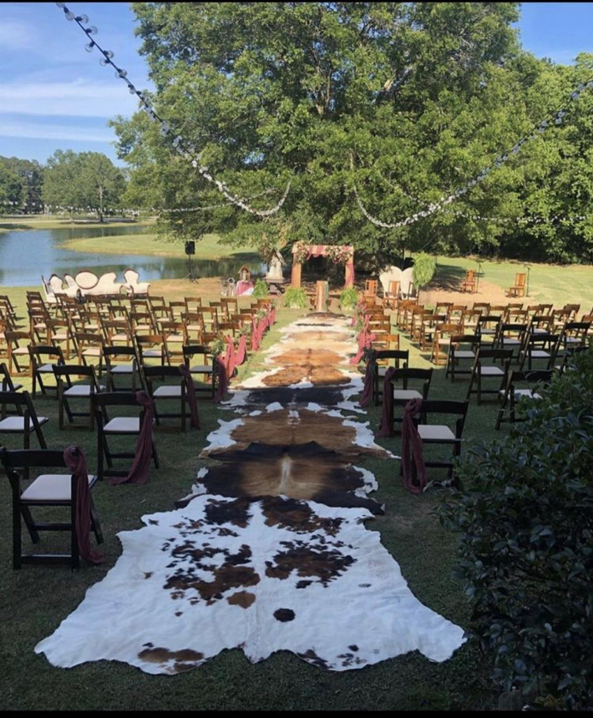 Cowhide rugs forming a rustic aisle runner between wooden chairs at an outdoor wedding.