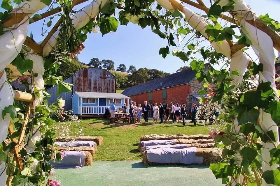 Hay bale seating with purple fabric covers in a rustic outdoor wedding setting.
