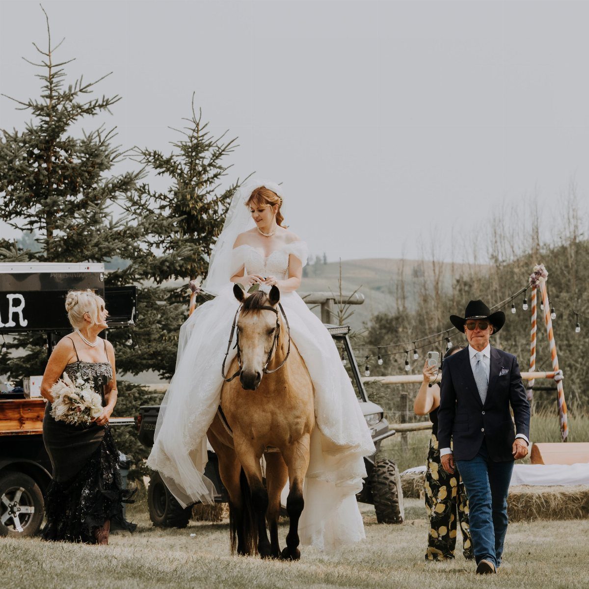 Bride in a white wedding dress riding a light brown horse in a field.