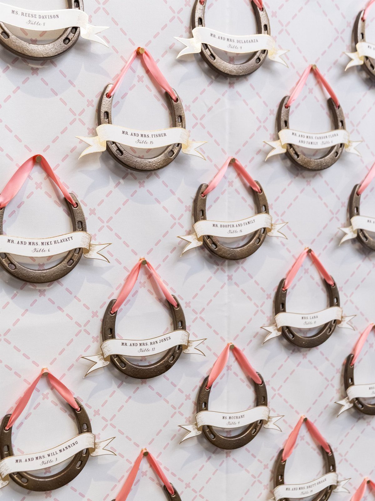 Horseshoes with name ribbons hanging on a white patterned wall as escort cards.